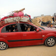 Palestinians in a red car loaded on top with mattresses and other supplies