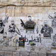 A mural depicting seven armed men is on the stone wall of a building 