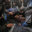 A kneeling man cradles and puts his head next to the face of a small child in a body bag as other men kneel and stand around him