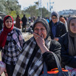 A woman holds her hand to her face while crying as she and other women carry tote bags while walking on street