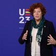 Belgian Deputy Prime Minister Petra De Sutter makes hands gestures in front of a blue backdrop 