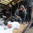 Two young men kneel next to shrouded bodies while a third leans onto and embraces a shrouded body