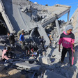 A girl stands in the foreground of a group of people on top of the rubble of a destroyed building