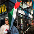 Portrait of a demonstrator with a Palestinian flag painted on her face and a placard in the shape of Palestine in front of a McDonald's restaurant
