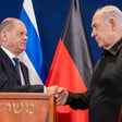 Scholz and Netanyahu shake hands by podiums with Israeli and German flags behind