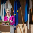 European Commission President Ursula von der Leyen stands in front of a few flags
