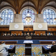 Judges sit at a long table below stained-glass windows in wood-paneled courtroom