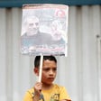 A boy holds a poster with a man and Arabic text on it 