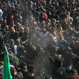 Man is carried on the shoulders of men in a big crowd of people carrying flags and weapons