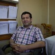 Man gives slight smile to camera while sitting on chair with his hands folding in his lap