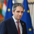 Ireland's Prime Minister Simon Harris stands before flags bearing the European Union's emblem