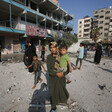 A woman holds a toddler while standing in front of damaged school