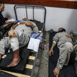 Men with bandaged arms and legs wearing grey prison clothes seen lying down
