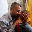 A man with bloodied hands cries while holding the head of an adolescent boy up to his face