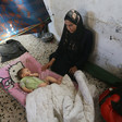 A woman sits against a wall, touching her sleeping infant. 