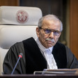 Man wearing judge's robe leans forward while sitting in front of microphone