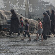 Four women and three children, most wearing sandals, walk along muck-covered road