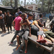 Four Palestinian men and boys, some of them streaked with blood, sit and lay on a donkey-drawn cart as bystanders look on