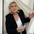Marine Le Pen pushing a curtain away and holding a mobile phone in her other hand 