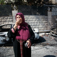 A woman stands in the street near burned vehicles 