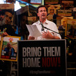 Steffen Seibert stands at a lectern surrounded by people carrying signs supporting Israelis held in Gaza