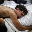 Close-up of a young man with an anguished face embracing a shrouded body