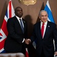 Two men in suits shaking hands in front of the British and Israeli flags