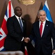 Two men in suits shaking hands in front of the British and Israeli flags