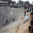 Boys look at camera as people stand on edge of sandy crater