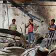 Three children stand on the charred and twisted ruins of shelters hit by an Israeli airstrike.