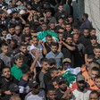 A large crowd carries corpses on stretchers wrapped in flags.