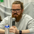 A man holds up and speaks into a microphone sitting between two people