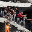 A group of people, some of them wearing orange civil defense vests, work to pull people out of the rubble of a destroyed building