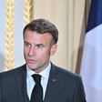 French President Emmanuel Macron stands with a flag behind him 