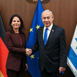 German Foreign Minister Annalena Baerbock clasps hands with Israeli Prime Minister Benjamin Netanyahu in front of German, European Union and Israeli flags 