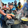 A boy looks at the camera while standing close to other boys and men holding pots over a vat of soup