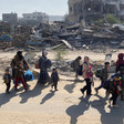 Families with young children carry their belongings past piles of rubble and wreckage