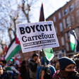 Woman carries sign as others behind her hold Palestinian flags and signs