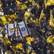 Football fans in a stadium wave yellow and Israeli flags