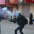 An armed and masked man points his rifles amid a cloud of smoke 