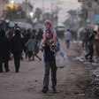 A young woman carries a toddler on her shoulders and holds a bag