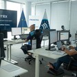 Two men sit behind computer screens and a banner reading Frontex European Border and Coast Guard Agency