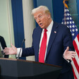 President Donald Trump with hands upraised at podium with man and American flag in background