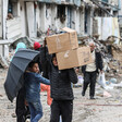 A boy holding an umbrella looks at another boy who is carrying boxes on his shoulders