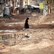 A girl walks amid muddy, damaged roads 