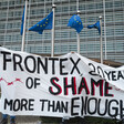 A banner reading Frontex 20 Years of Shame More than Enough beneath the European Union's flags at a protest in Brussels