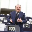 An Italian lawmaker wearing a suit gestures with his hands as he stands and speaks at a podium inside the European Parliament 