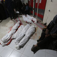 A woman sits on the floor leaning against a wall next to the shrouded bodies of several children