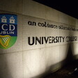 A sign which is partly illuminated and partly covered with shadows and which bears the logo of University College Dublin