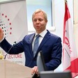 Diplomat wearing a suit stands at a lectern with two flags behind him 